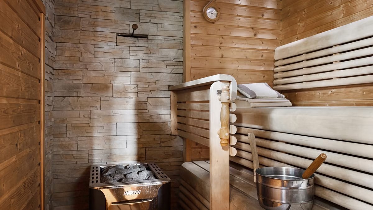Featuring a relaxing sauna interior with wooden benches and a stone wall heater for a serene escape.